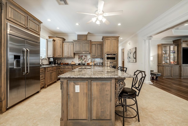 kitchen with sink, a center island with sink, decorative columns, and appliances with stainless steel finishes