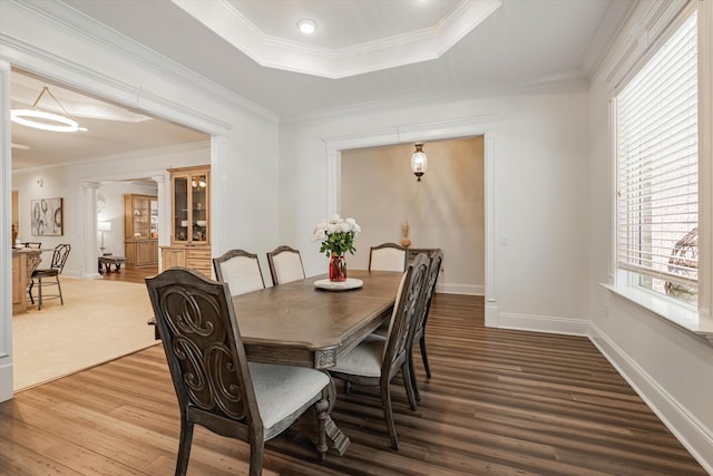 dining room with crown molding, a tray ceiling, hardwood / wood-style floors, and decorative columns