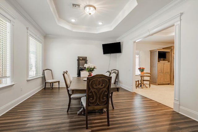 dining space with dark hardwood / wood-style floors, ornamental molding, a raised ceiling, and a healthy amount of sunlight