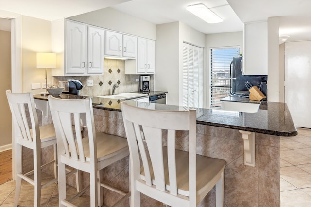 kitchen with decorative backsplash, kitchen peninsula, white cabinets, and a kitchen bar