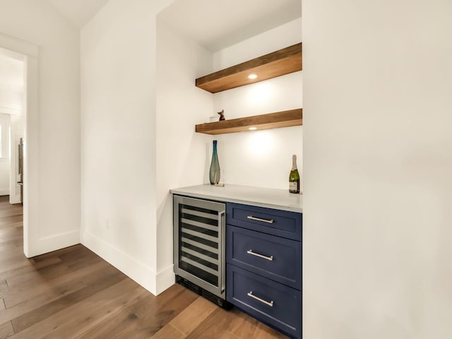 bar with dark hardwood / wood-style floors, blue cabinets, and beverage cooler