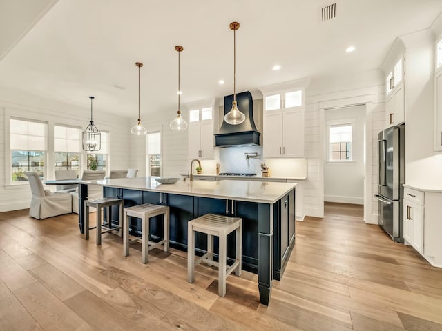 kitchen featuring premium range hood, pendant lighting, high end fridge, and a large island with sink