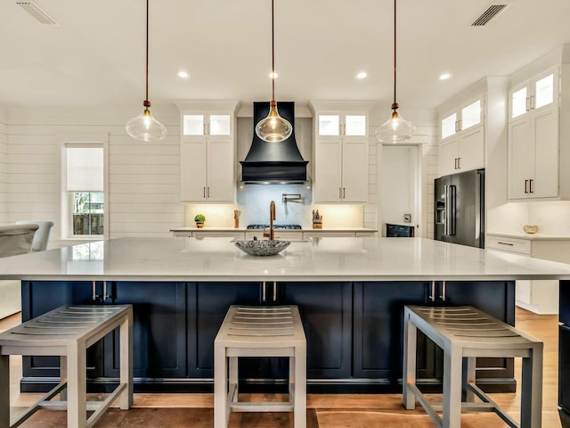 kitchen featuring premium range hood, pendant lighting, high end refrigerator, and white cabinets