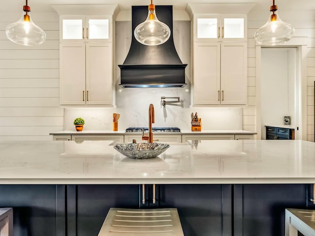 kitchen featuring light stone countertops, hanging light fixtures, and custom exhaust hood