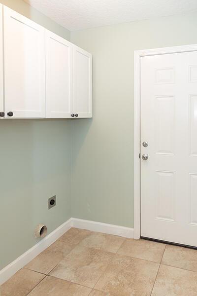 clothes washing area featuring cabinets, hookup for an electric dryer, a textured ceiling, and light tile patterned floors