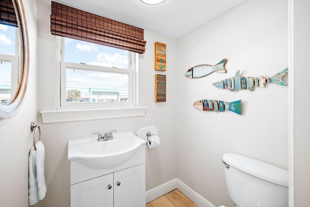 half bathroom with vanity, toilet, wood finished floors, and baseboards