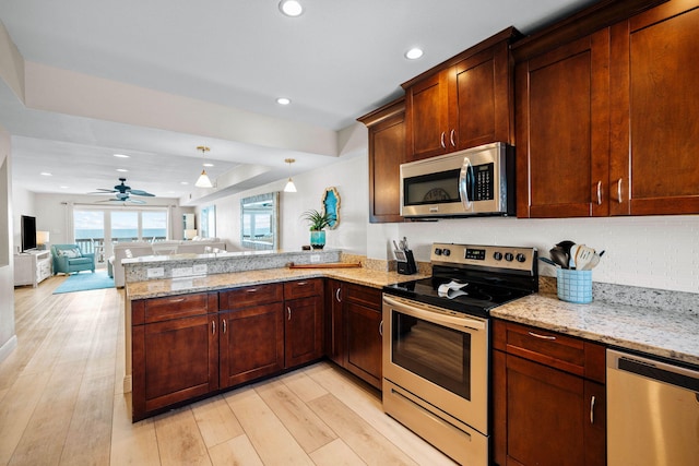 kitchen featuring open floor plan, light stone counters, appliances with stainless steel finishes, a peninsula, and light wood-style floors