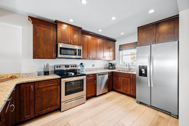 kitchen with light stone counters, light wood-style flooring, recessed lighting, a sink, and appliances with stainless steel finishes