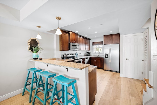 kitchen featuring a breakfast bar, a peninsula, light wood-style flooring, a sink, and stainless steel appliances