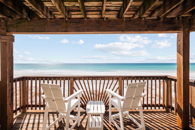 wooden terrace featuring a water view and a beach view