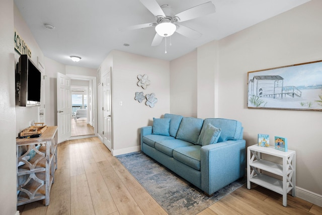 living area with baseboards, light wood-type flooring, and ceiling fan