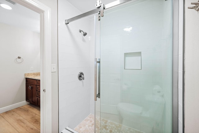 full bathroom with baseboards, wood finished floors, a stall shower, and vanity