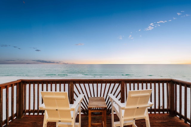 deck at dusk featuring a view of the beach and a water view