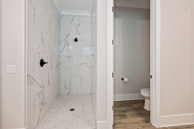 bathroom featuring a tile shower, hardwood / wood-style flooring, ornamental molding, and toilet