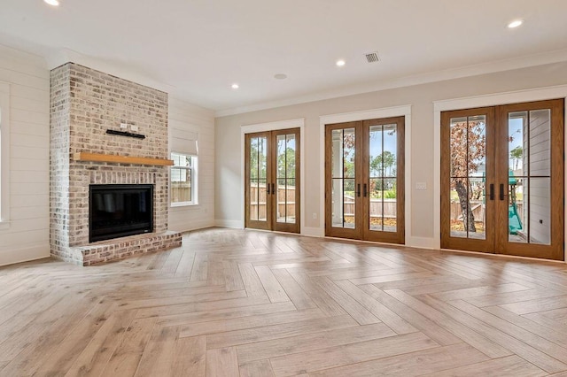 unfurnished living room featuring french doors, ornamental molding, light parquet flooring, and a brick fireplace