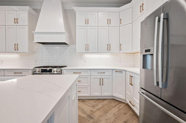 kitchen with light stone counters, custom range hood, white cabinets, stainless steel appliances, and backsplash