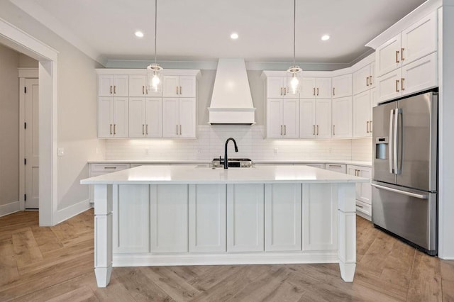 kitchen featuring hanging light fixtures, premium range hood, a center island with sink, and stainless steel fridge