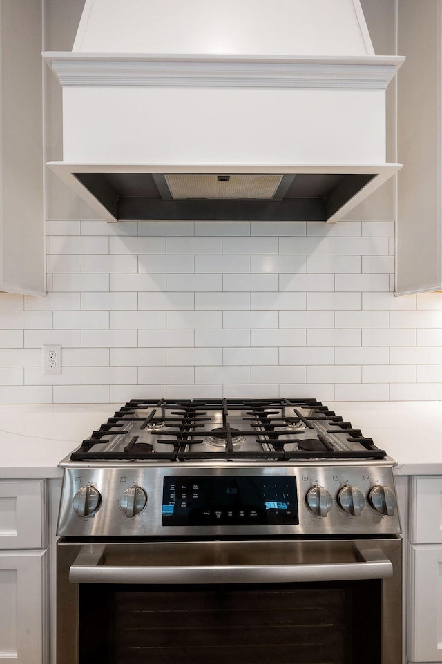 kitchen featuring white cabinetry, stainless steel gas range oven, premium range hood, and decorative backsplash