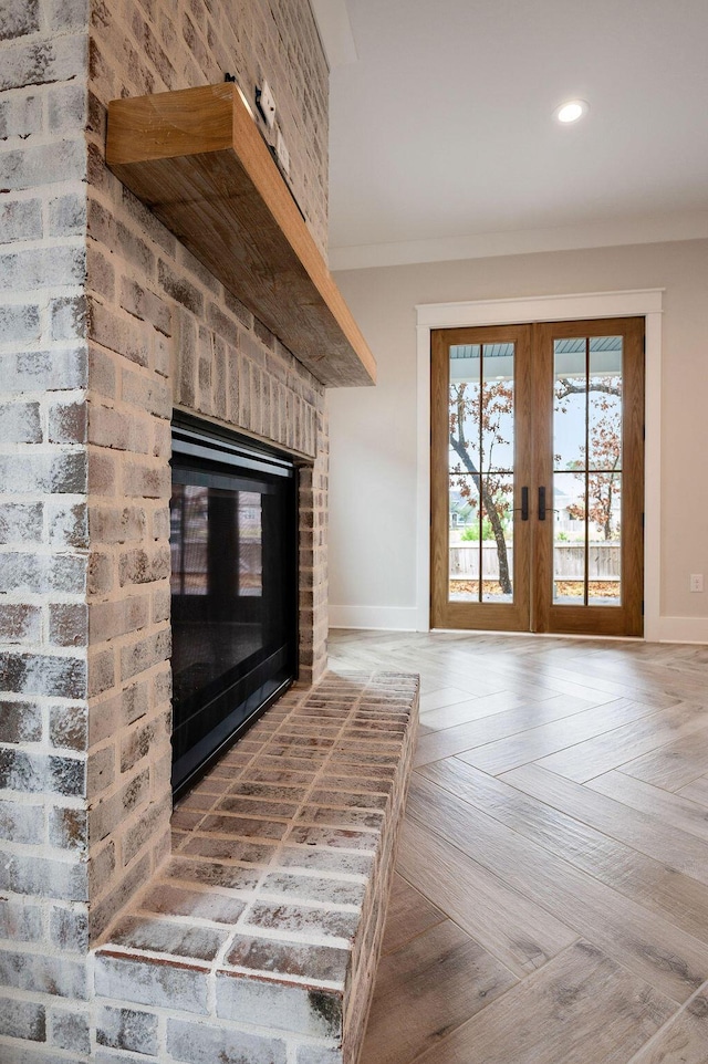 unfurnished living room with a brick fireplace, crown molding, wood-type flooring, and french doors