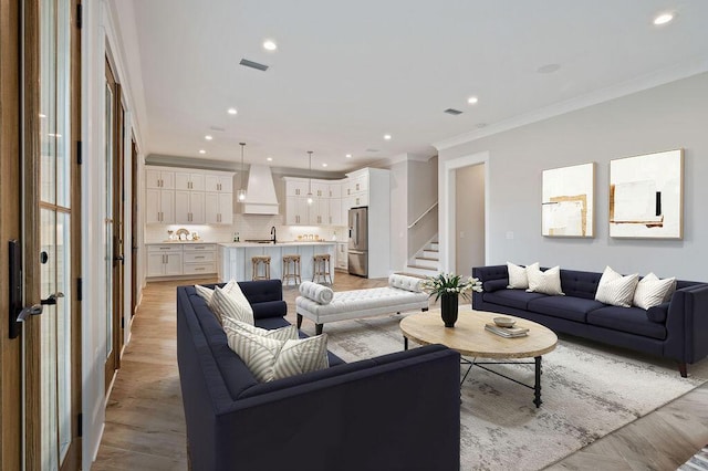 living room featuring crown molding, sink, and light hardwood / wood-style flooring