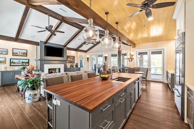 kitchen with dark wood-style flooring, butcher block counters, a kitchen island with sink, a sink, and a warm lit fireplace