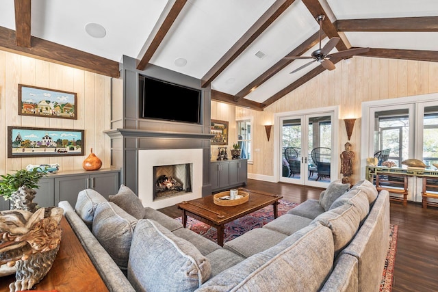 living area featuring plenty of natural light, a lit fireplace, dark wood-style floors, and french doors