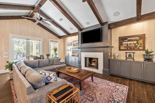 living area with dark wood-style floors, wooden walls, a lit fireplace, and lofted ceiling with beams