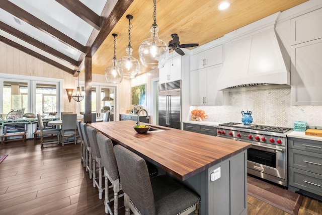 kitchen featuring premium appliances, butcher block counters, custom exhaust hood, gray cabinets, and a sink