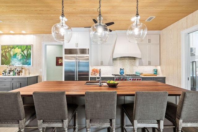 kitchen featuring wooden ceiling, custom range hood, wood counters, and appliances with stainless steel finishes