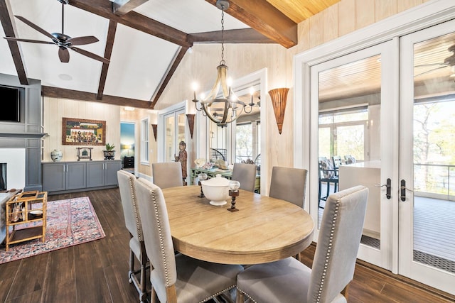 dining room featuring dark wood finished floors, lofted ceiling with beams, french doors, wood walls, and ceiling fan with notable chandelier