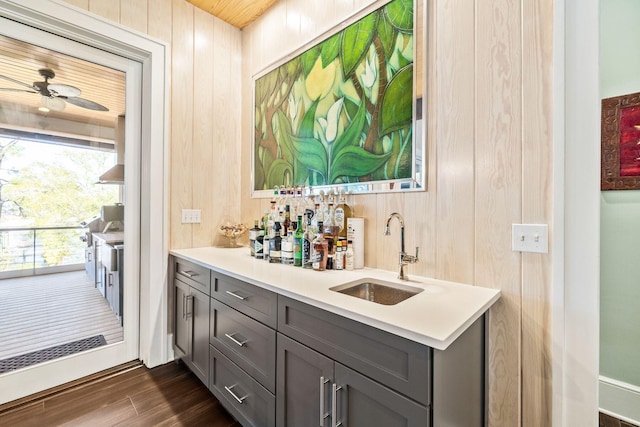 bar featuring a ceiling fan, dark wood-type flooring, a sink, wood walls, and indoor wet bar