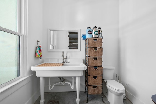 bathroom with baseboards, concrete floors, toilet, and a healthy amount of sunlight