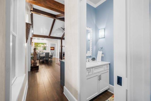 interior space with wood finished floors, a ceiling fan, vanity, baseboards, and beamed ceiling