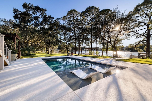 pool with a water view, a patio area, and a lawn