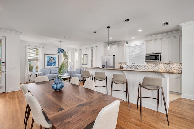 dining space with ornamental molding, sink, and light hardwood / wood-style flooring