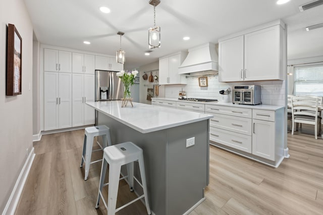 kitchen featuring custom exhaust hood, visible vents, decorative backsplash, appliances with stainless steel finishes, and a kitchen breakfast bar