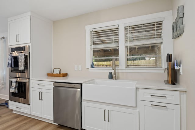 kitchen with a sink, white cabinets, light countertops, appliances with stainless steel finishes, and light wood finished floors