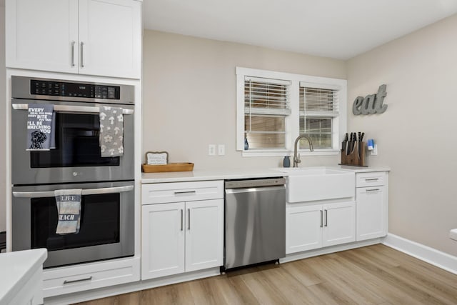 kitchen with stainless steel appliances, light wood-style floors, white cabinets, and a sink