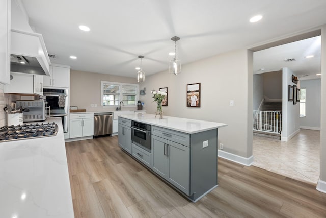 kitchen featuring stainless steel appliances, gray cabinets, custom exhaust hood, and light wood-style floors