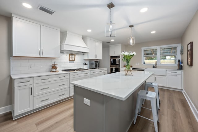 kitchen featuring custom exhaust hood, visible vents, appliances with stainless steel finishes, a kitchen island, and a sink