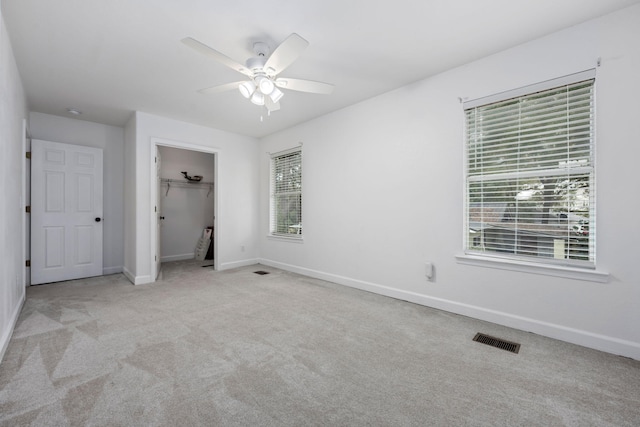 unfurnished bedroom featuring a walk in closet, visible vents, a ceiling fan, carpet flooring, and baseboards