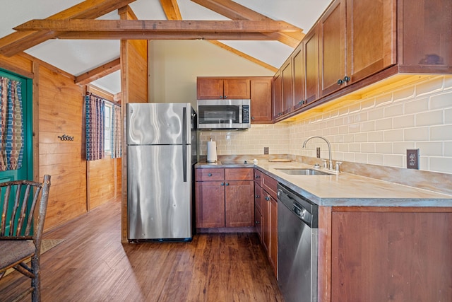 kitchen featuring vaulted ceiling with beams, light countertops, appliances with stainless steel finishes, brown cabinetry, and a sink