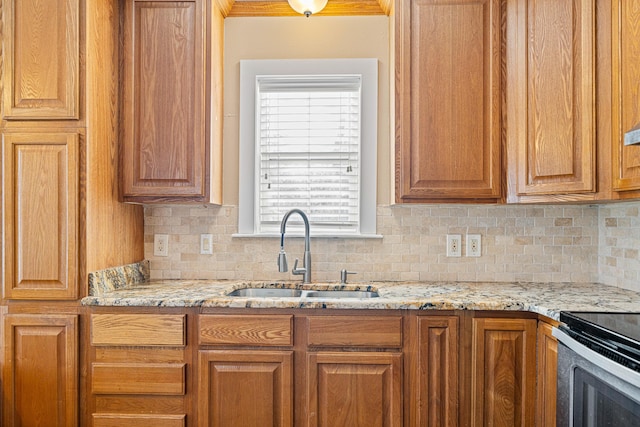 kitchen with electric range, light stone counters, brown cabinets, a sink, and backsplash