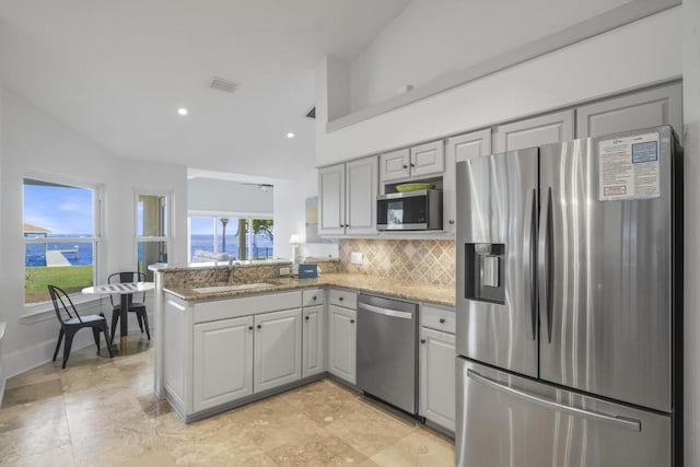 kitchen with a peninsula, stainless steel appliances, gray cabinetry, stone counters, and a sink