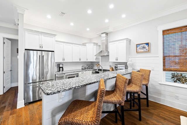 kitchen featuring white cabinets, a kitchen breakfast bar, light stone counters, stainless steel appliances, and wall chimney exhaust hood