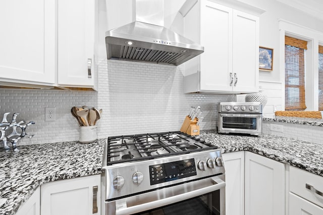 kitchen with stainless steel gas range, white cabinetry, backsplash, dark stone countertops, and exhaust hood