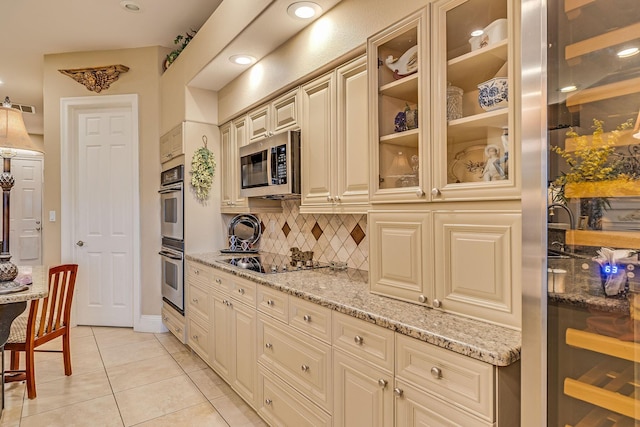 kitchen with light tile patterned floors, stainless steel appliances, light stone counters, cream cabinets, and decorative backsplash