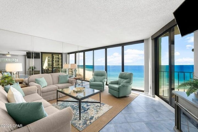 living room with light tile patterned flooring, a wall of windows, a water view, a beach view, and a textured ceiling