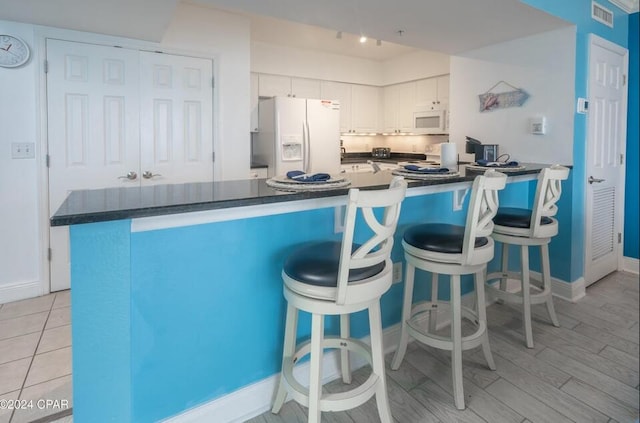 kitchen with white cabinetry, a kitchen bar, kitchen peninsula, white appliances, and light hardwood / wood-style flooring