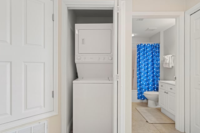 laundry area with stacked washer and dryer and light tile patterned flooring